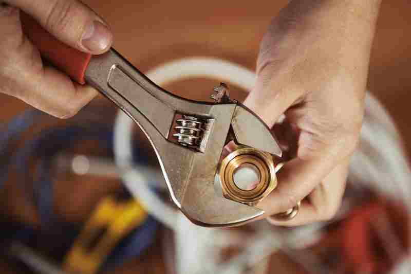 Close-up of plumber hands screwing nut of pipe with wrench over