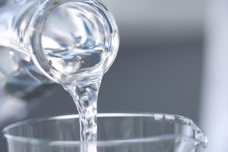 Scientist chemist in gloves pouring water from flask into glass closeup