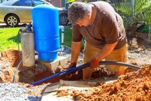 man works on installing plumbing system next to blue tank in home under connect to water well