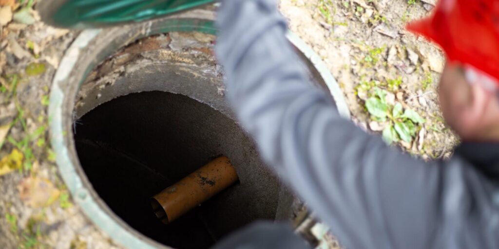 a worker leans over a septic tank, showing a sewage drain pipe