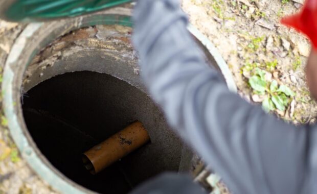 a worker leans over a septic tank, showing a sewage drain pipe