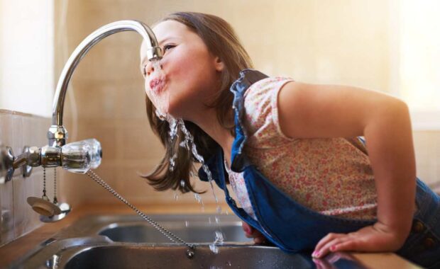 Shot of a little girl drinking water directly from the kitchen tap at home.