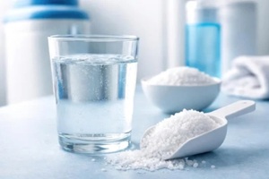 glass of water with salt scoop used in process of reducing water hardness through softening agents