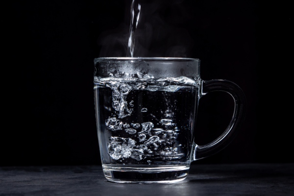 Boiling water is poured into a glass on a black background. Hot drinking water