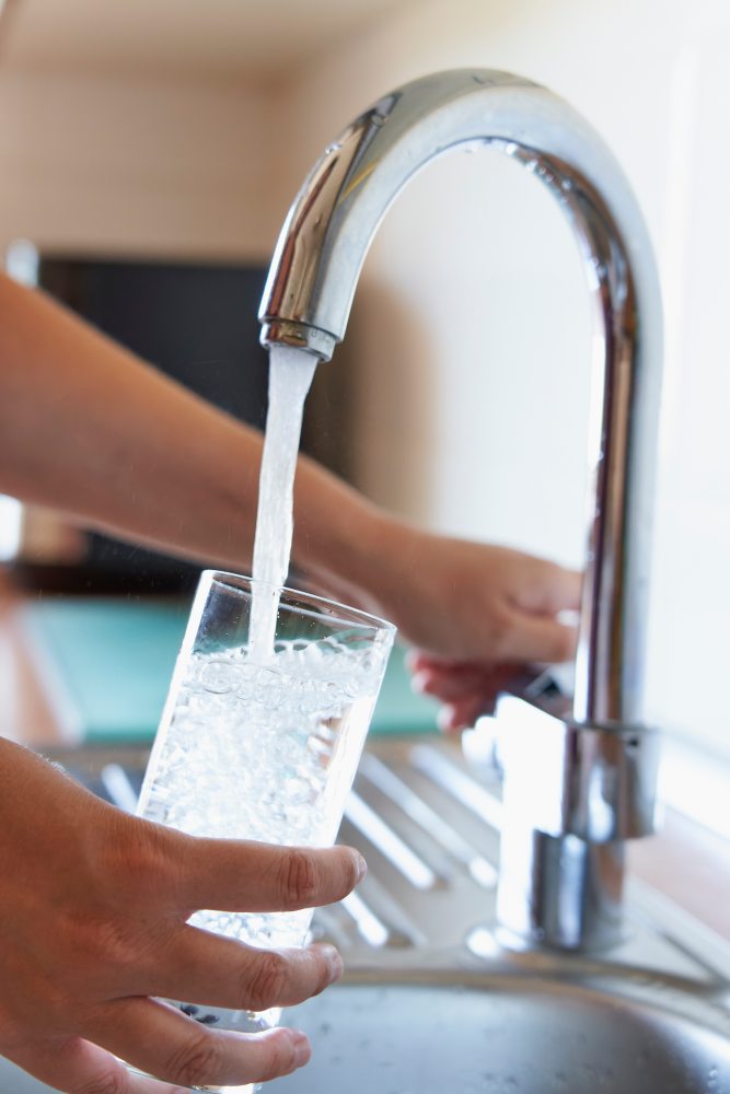 Woman filling glass of cool water at kitchen faucet
