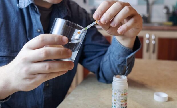 man in the kitchen tests tap water quality with a test strip