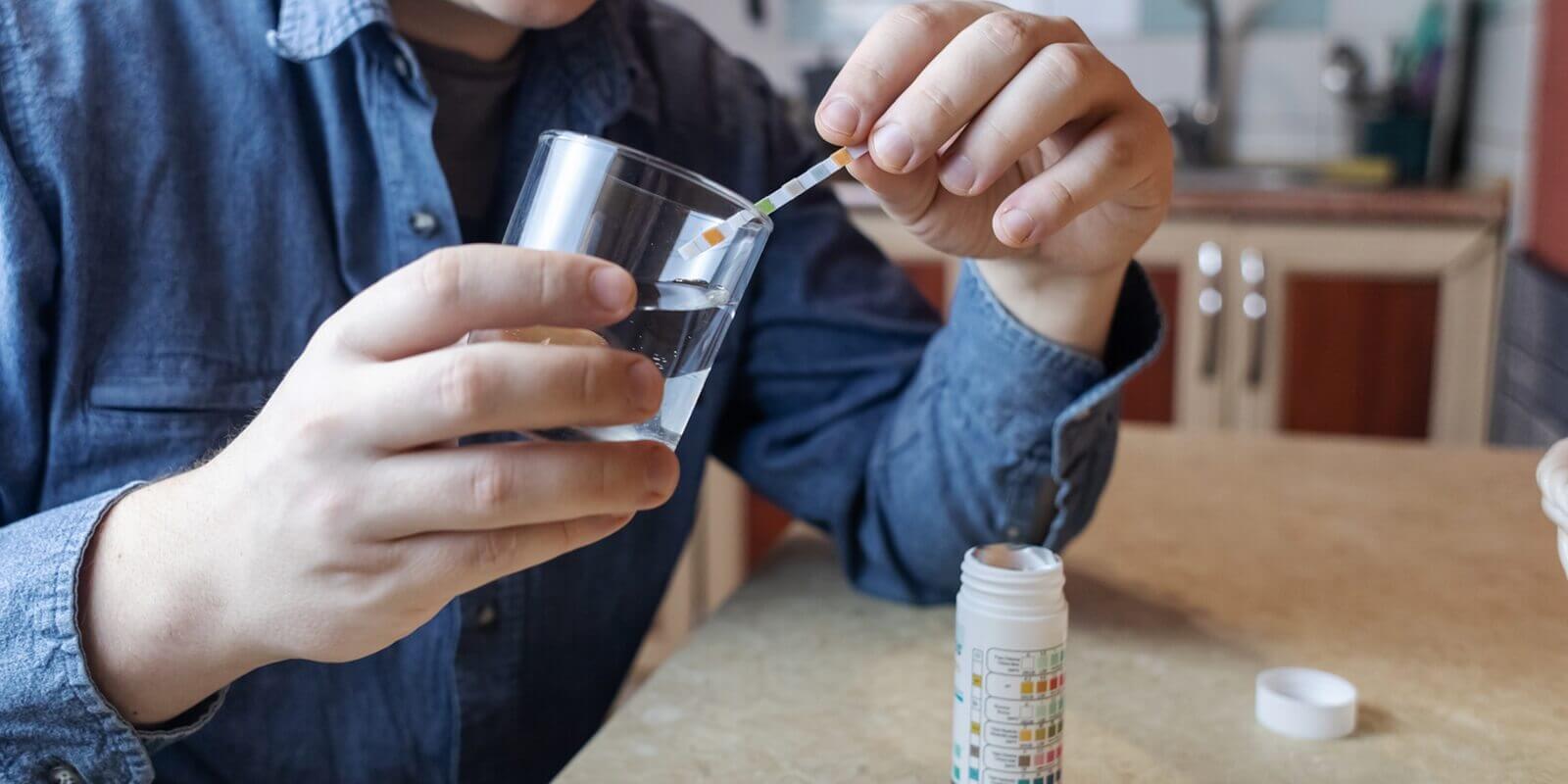 man in the kitchen tests tap water quality with a test strip