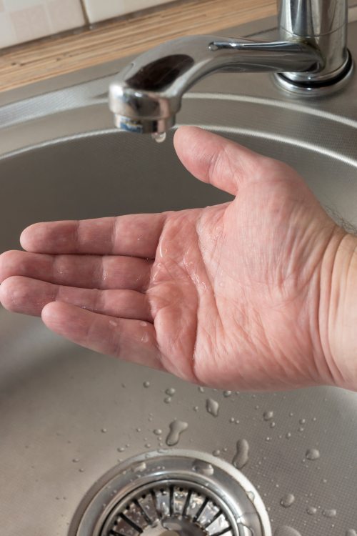 A drop of water drips in mans palm who checks if there is water in kitchen tap
