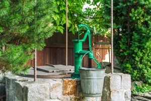 stone water well with an old metal bucket in green garden