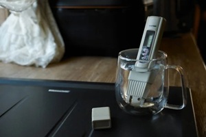 water quality analyzer (salt meter) that measures the total amount of substances dissolved in water placed in a glass of water on a wooden table