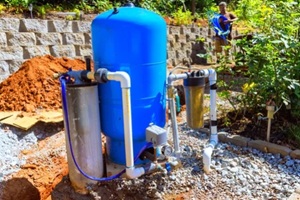 workers set up artesian water well system in garden surrounded by gravel