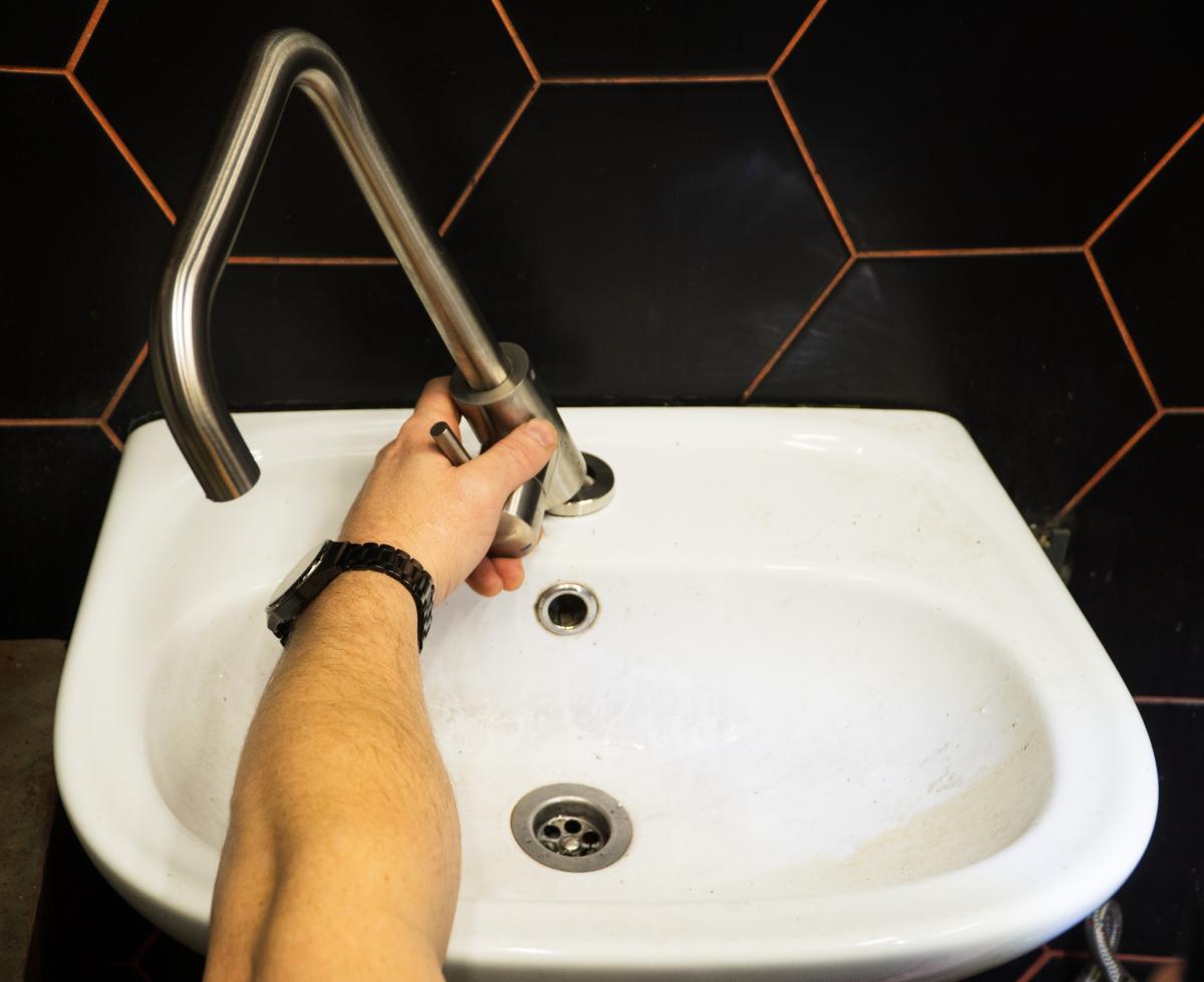 Plumber changes broken, leaking plumbing fixtures in the bathroom. Repair of a water tap. Plumber uses a wrench to install the faucet in the bathroom. An adult man changes the faucet in the kitchen.