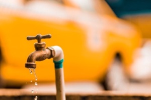 brass faucet with water droplets against a blurred yellow background