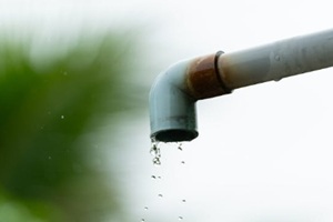 close-up of water droplets falling from a rusty outdoor pipe against a blurred natural background