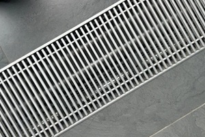 modern metal linear drain grate with parallel bars on a dark grey textured floor surface