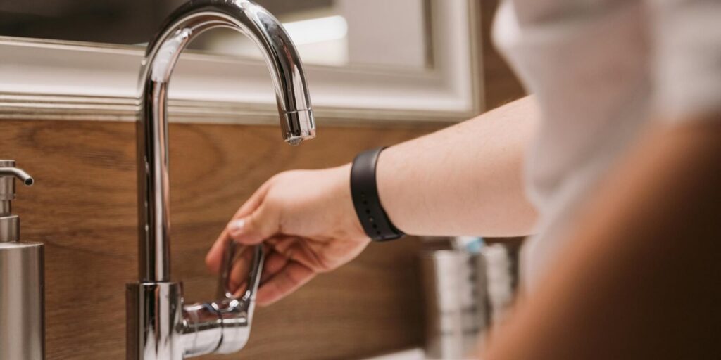 person's hand turning a chrome faucet handle in a modern bathroom setting