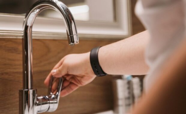 person's hand turning a chrome faucet handle in a modern bathroom setting