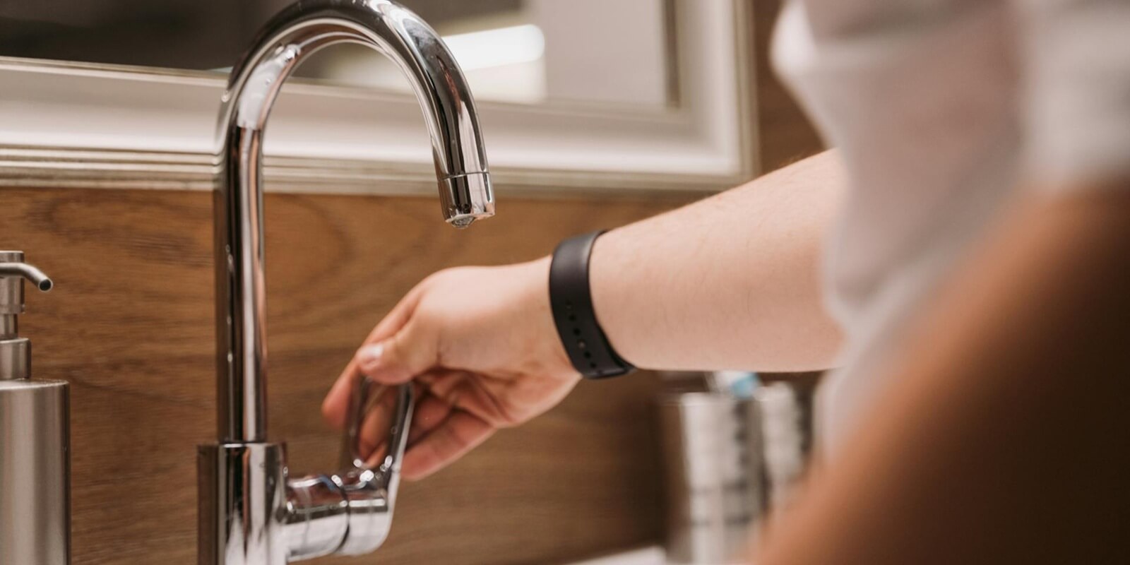 person's hand turning a chrome faucet handle in a modern bathroom setting
