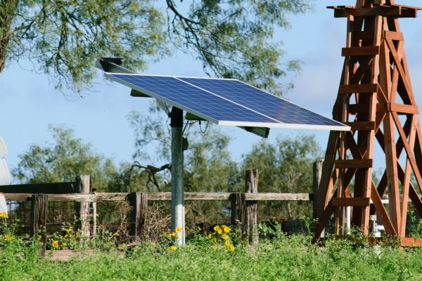 Solar Water well with Texas Windmill, in front of a green beautiful tree, with old vintage windmill on ground in front of fence.