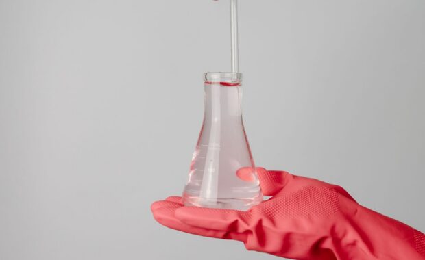 laboratory scene showing red-gloved hands holding a flask with clear liquid