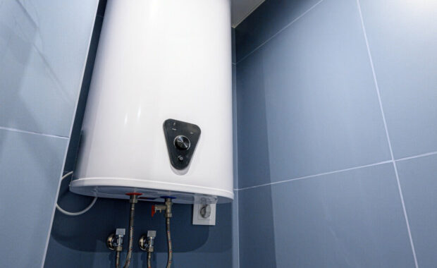 white electric water heater mounted on blue tiled wall in bathroom, with control knob, water inlet outlet pipes