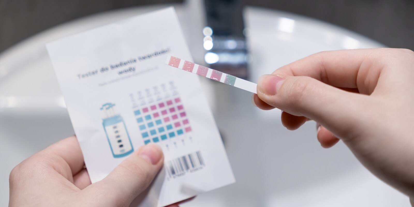 hands holding a water hardness test strip with comparison chart